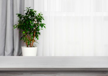 Image of Empty white wooden table near window with curtains and houseplant. Space for design