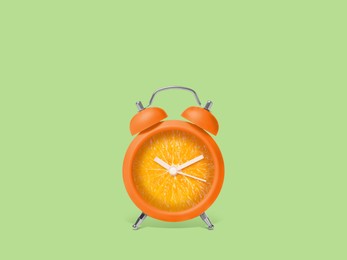 Juicy orange on alarm clock dial against light green background. Creative poster