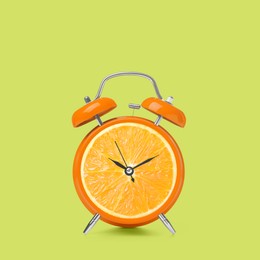 Image of Juicy orange on alarm clock dial against light green background. Creative poster