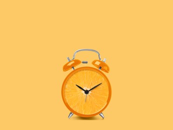 Juicy orange on alarm clock dial against light orange background. Creative poster