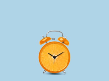 Juicy orange on alarm clock dial against light blue background. Creative poster