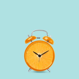 Juicy orange on alarm clock dial against light blue background. Creative poster