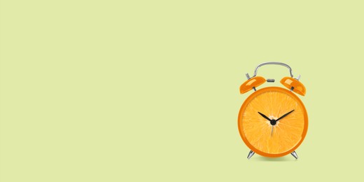 Image of Juicy orange on alarm clock dial against light green background. Creative poster with space for text, banner design