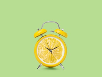 Image of Juicy lemon on alarm clock dial against light green background. Creative poster