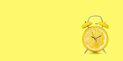 Image of Juicy lemon on alarm clock dial against light yellow background. Creative poster with space for text, banner design