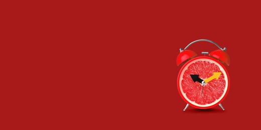 Image of Juicy grapefruit on alarm clock dial against red background. Creative poster with space for text, banner design