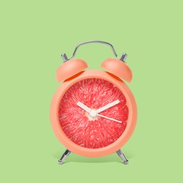 Image of Juicy grapefruit on alarm clock dial against light green background. Creative poster