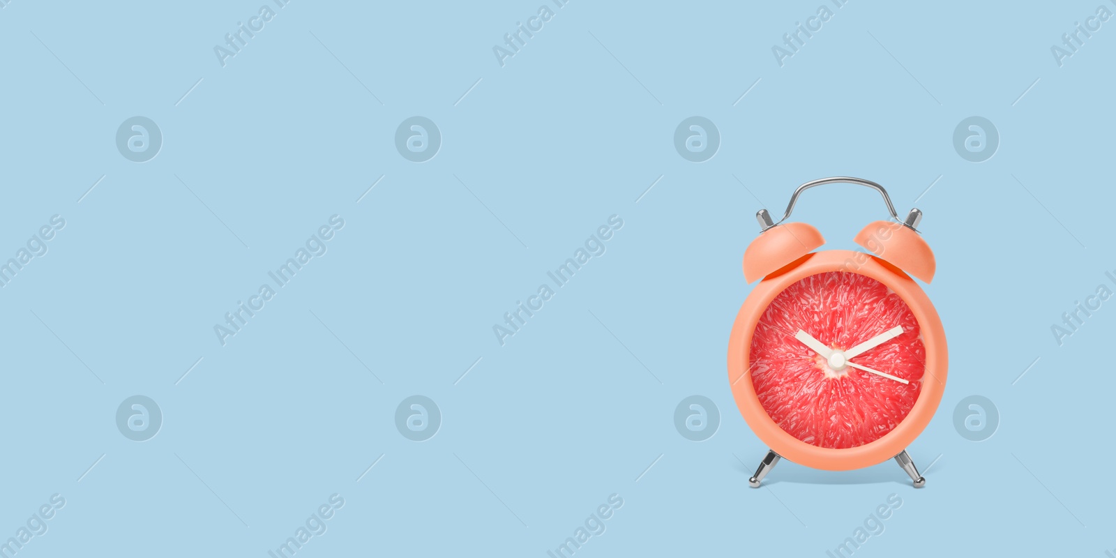 Image of Juicy grapefruit on alarm clock dial against light blue background. Creative poster with space for text, banner design