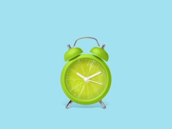 Juicy lime on alarm clock dial against light blue background. Creative poster