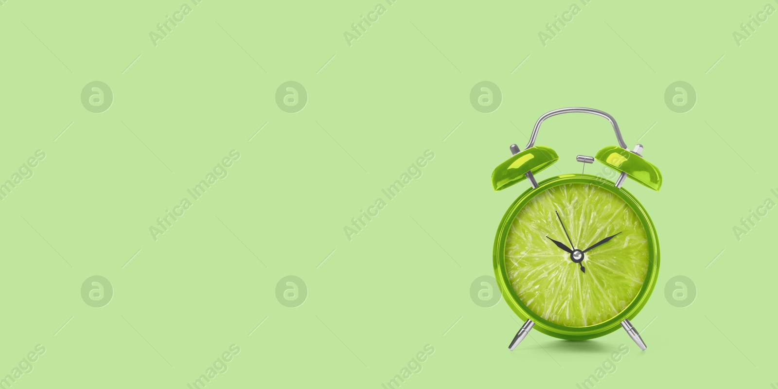 Image of Juicy lime on alarm clock dial against light green background. Creative poster with space for text, banner design