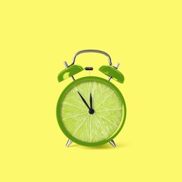 Image of Juicy lime on alarm clock dial against light yellow background. Creative poster