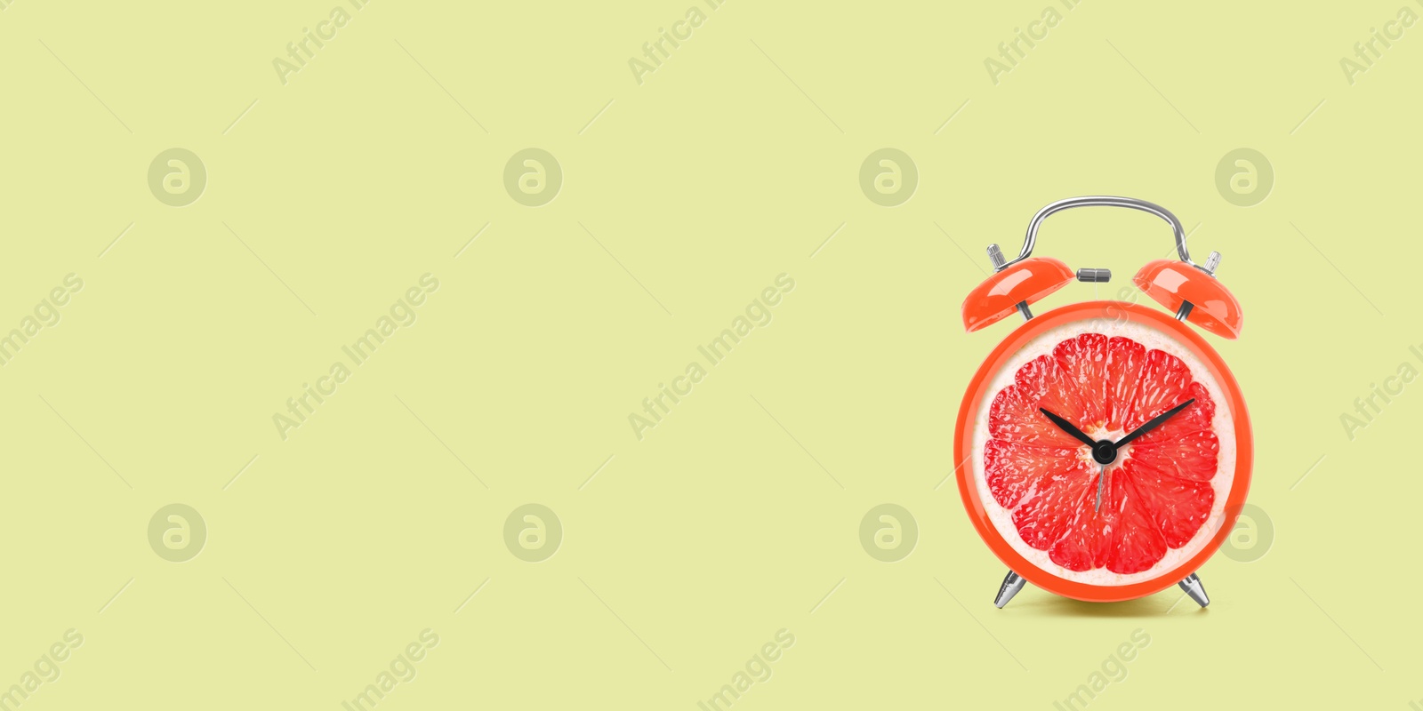 Image of Juicy grapefruit on alarm clock dial against light green background. Creative poster with space for text, banner design