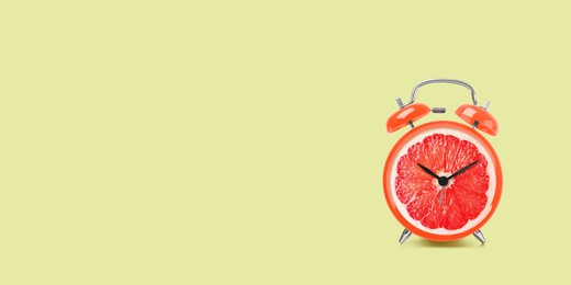 Image of Juicy grapefruit on alarm clock dial against light green background. Creative poster with space for text, banner design