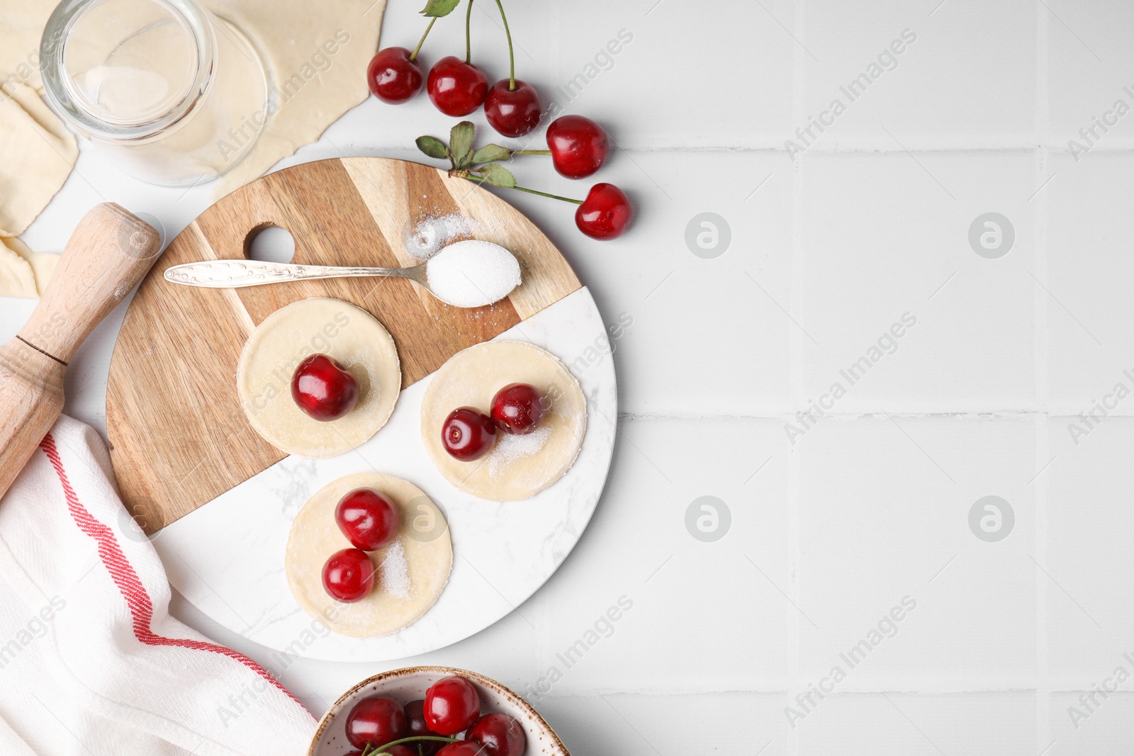 Photo of Process of making dumplings (varenyky) with cherries. Raw dough and ingredients on white tiled table, flat lay. Space for text