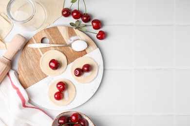 Photo of Process of making dumplings (varenyky) with cherries. Raw dough and ingredients on white tiled table, flat lay. Space for text