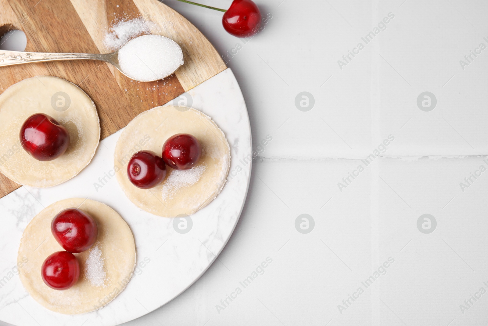 Photo of Process of making dumplings (varenyky) with cherries. Raw dough and ingredients on white tiled table, flat lay. Space for text