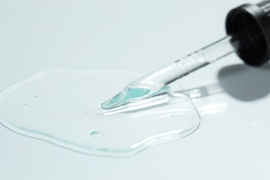 Pipette with cosmetic serum on light background, closeup