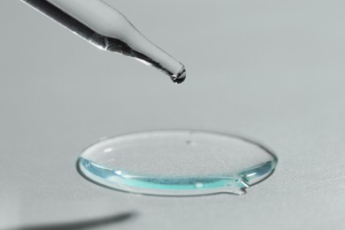 Photo of Dripping cosmetic serum from pipette on light background, closeup