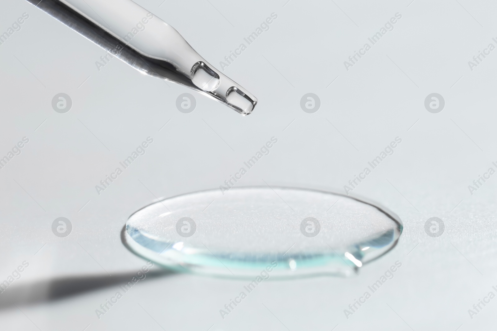 Photo of Dripping cosmetic serum from pipette on light background, closeup