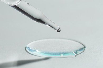 Photo of Dripping cosmetic serum from pipette on light background, closeup