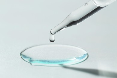 Photo of Dripping cosmetic serum from pipette on light background, closeup