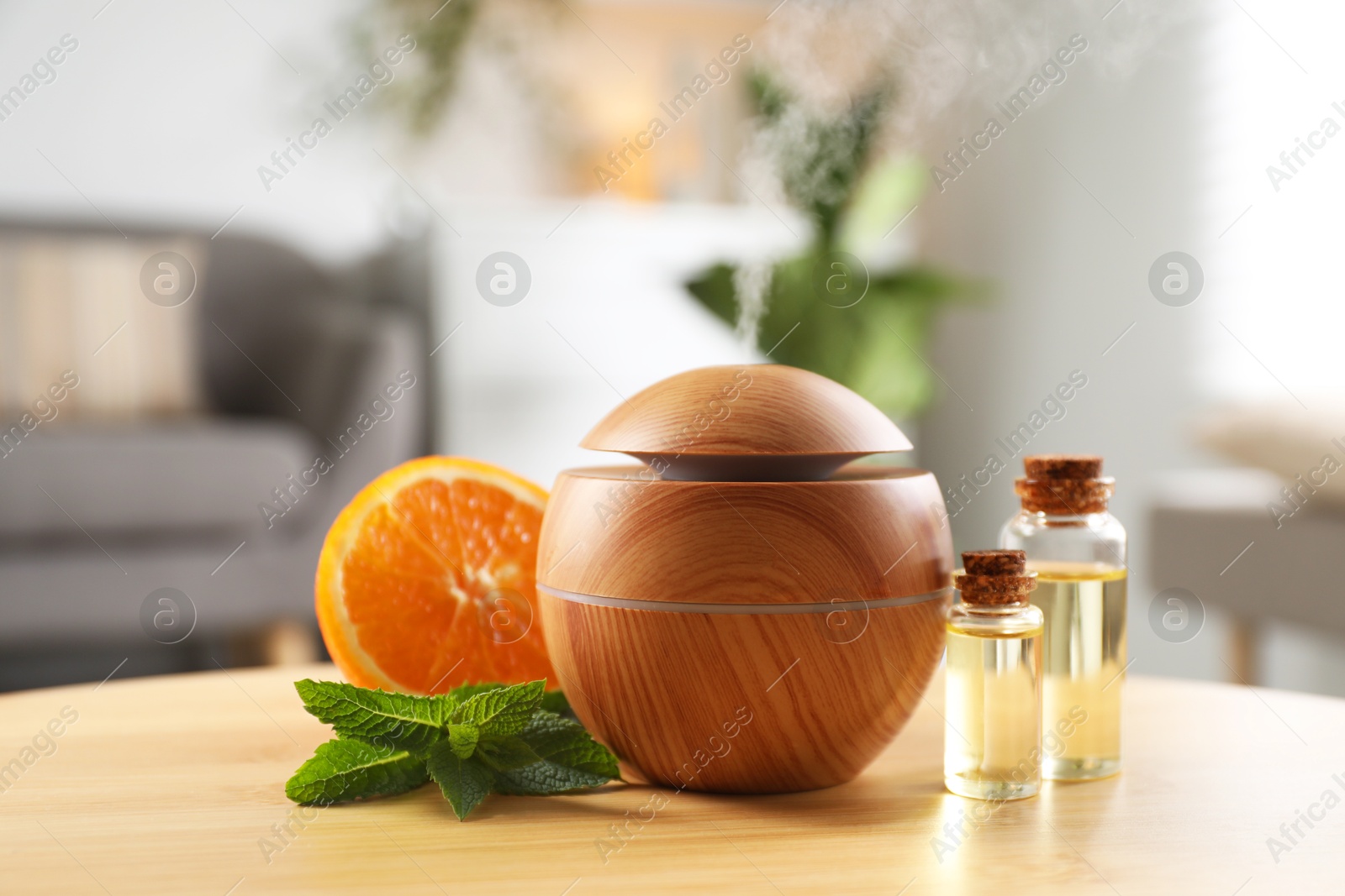 Photo of Essential oil diffuser, cosmetic products, mint and orange on wooden table at home