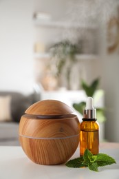 Photo of Essential oil diffuser, cosmetic product and mint on white table at home