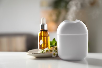 Photo of Essential oil diffuser, cosmetic product and chamomile flowers on white table at home