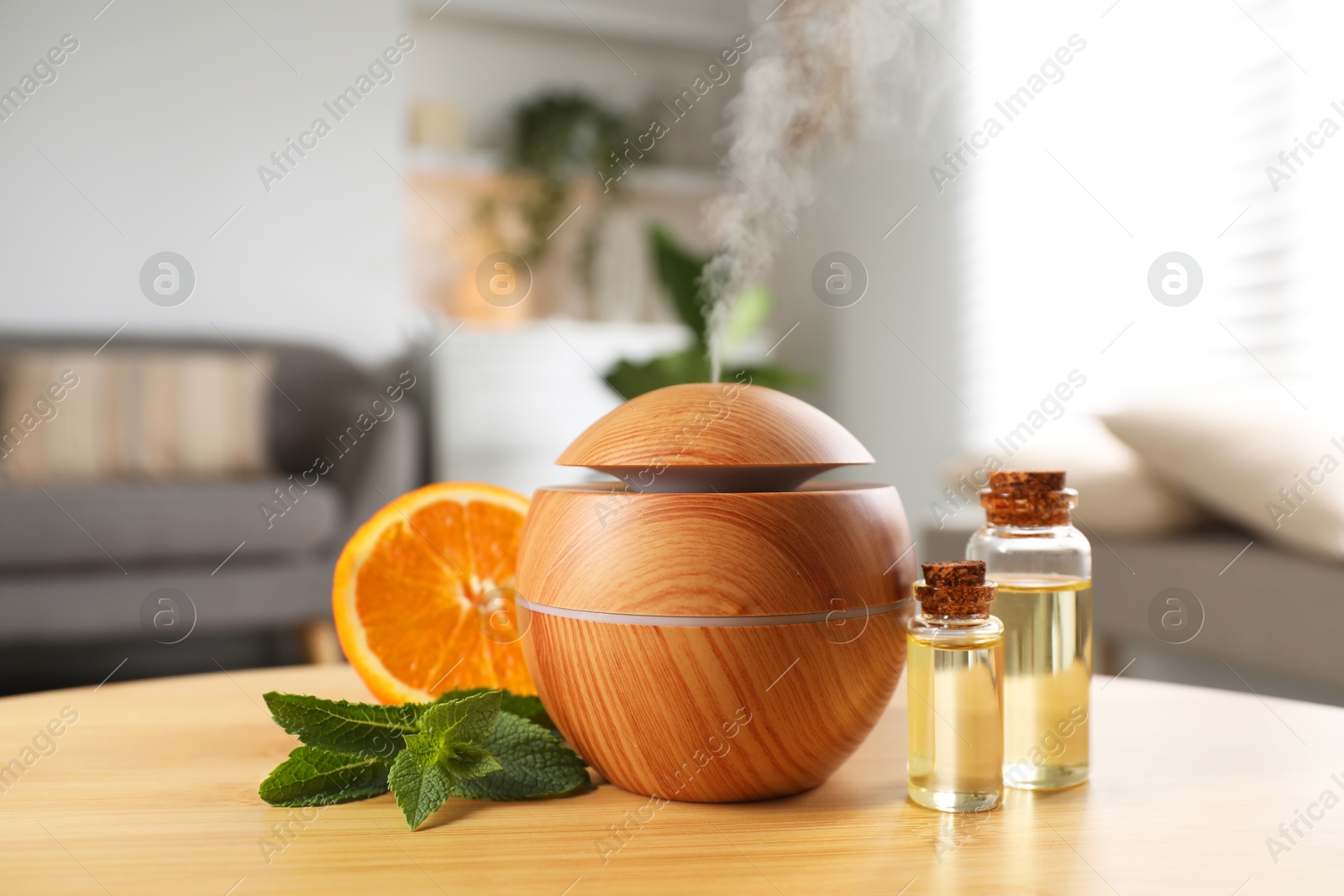 Photo of Essential oil diffuser, cosmetic products, mint and orange on wooden table at home