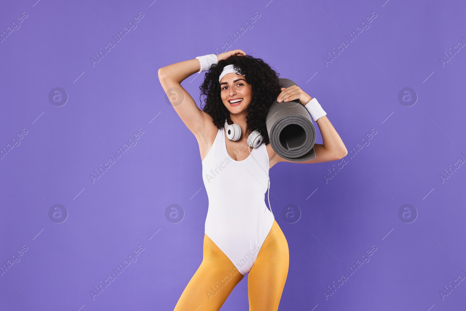 Photo of Woman with headphones and fitness mat on purple background