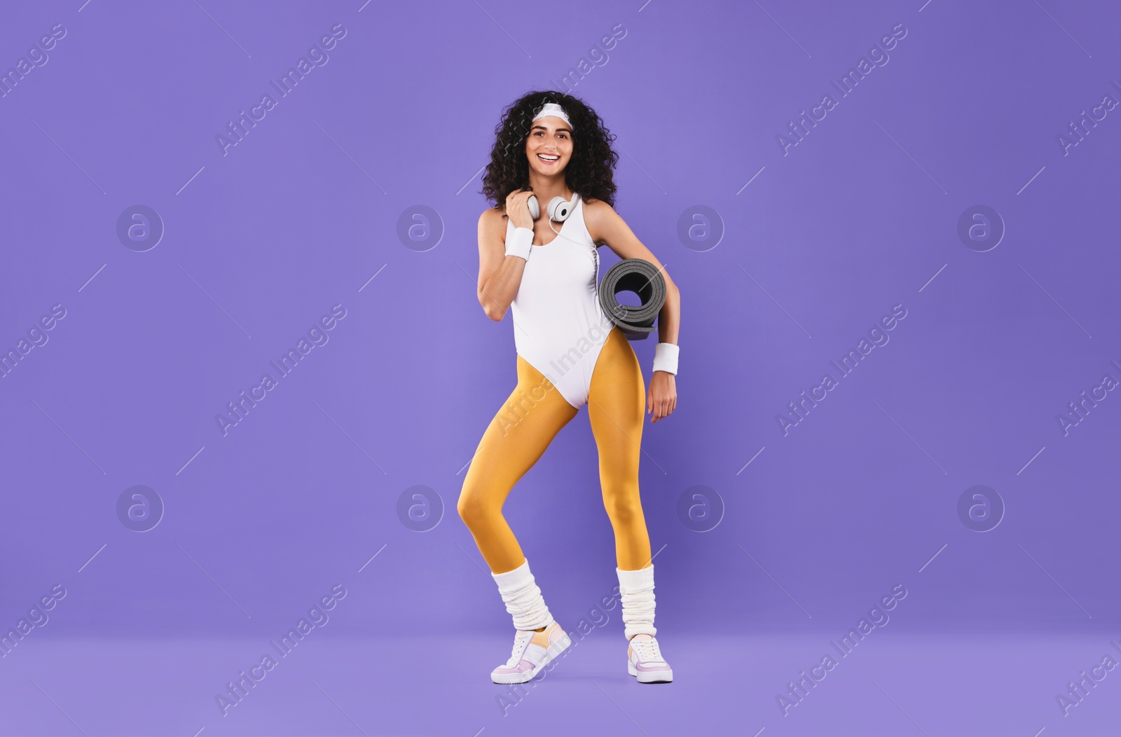 Photo of Woman with headphones and fitness mat on purple background