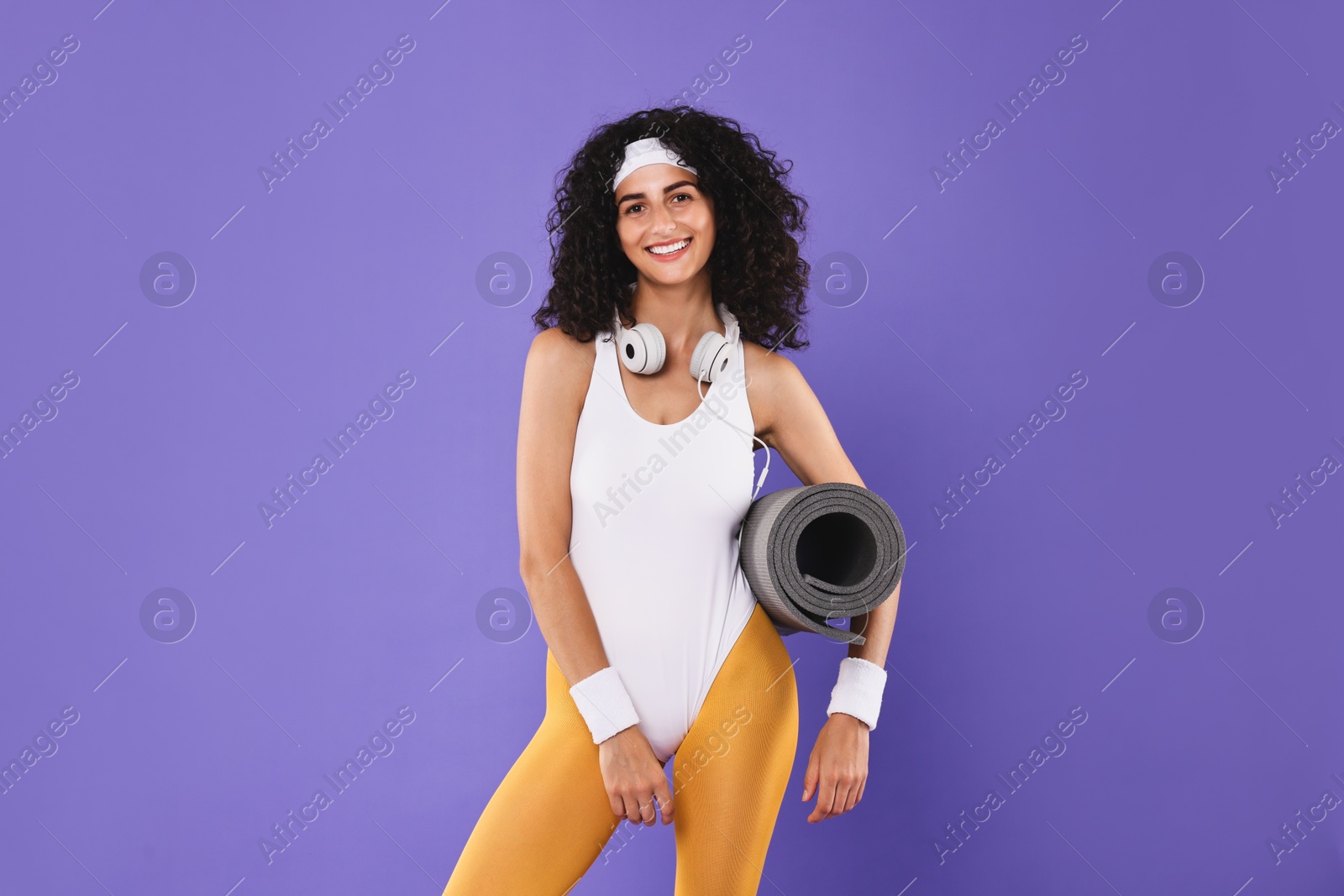 Photo of Woman with headphones and fitness mat on purple background