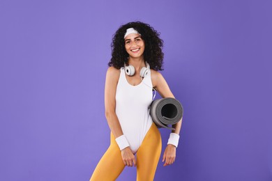 Woman with headphones and fitness mat on purple background