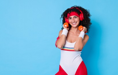 Woman in headphones doing aerobic exercise with dumbbells on light blue background, space for text