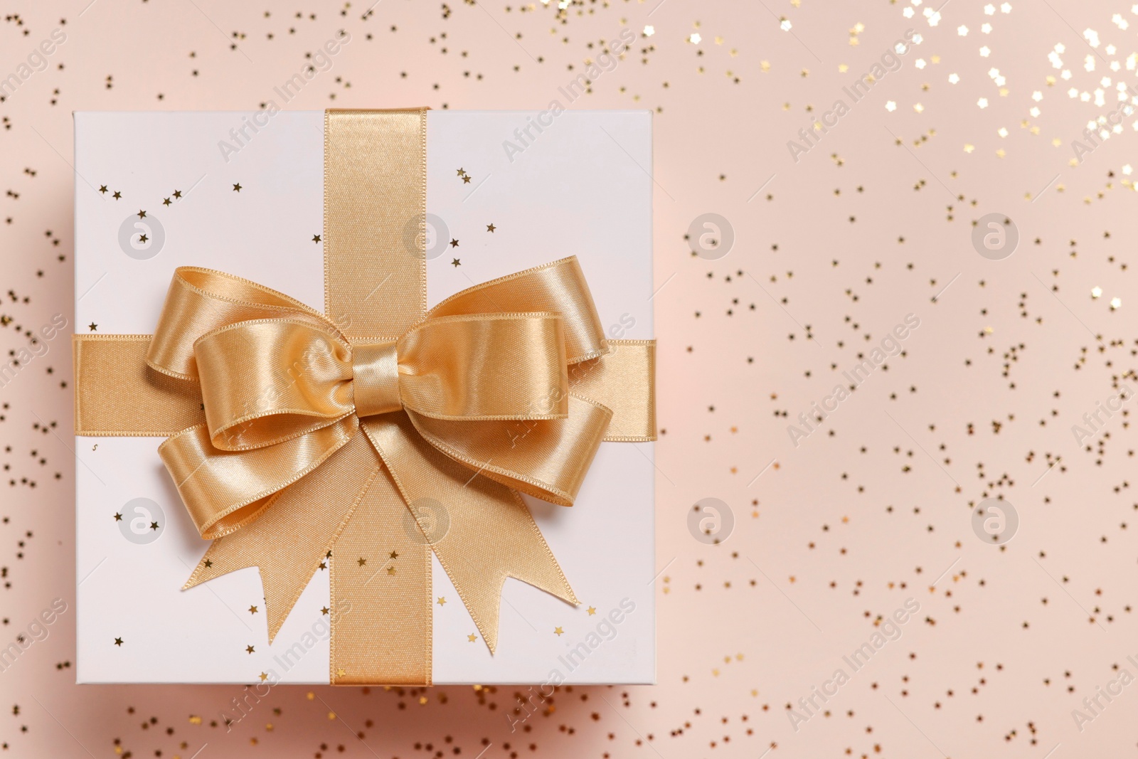 Photo of Gift box with bow and confetti on beige background, top view