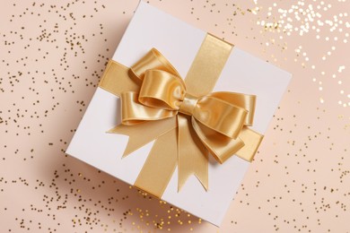 Gift box with bow and confetti on beige background, top view