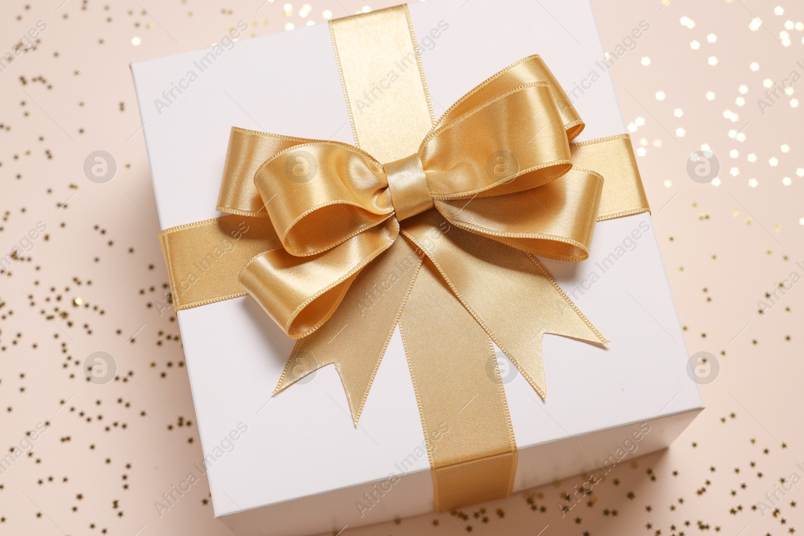 Photo of Gift box with bow and confetti on beige background, closeup