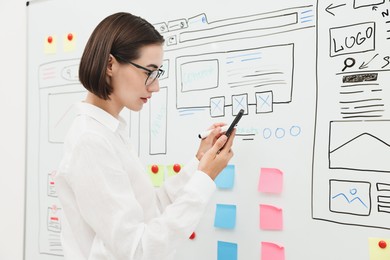 Photo of Developing UI design. Woman drawing website wireframe on whiteboard indoors