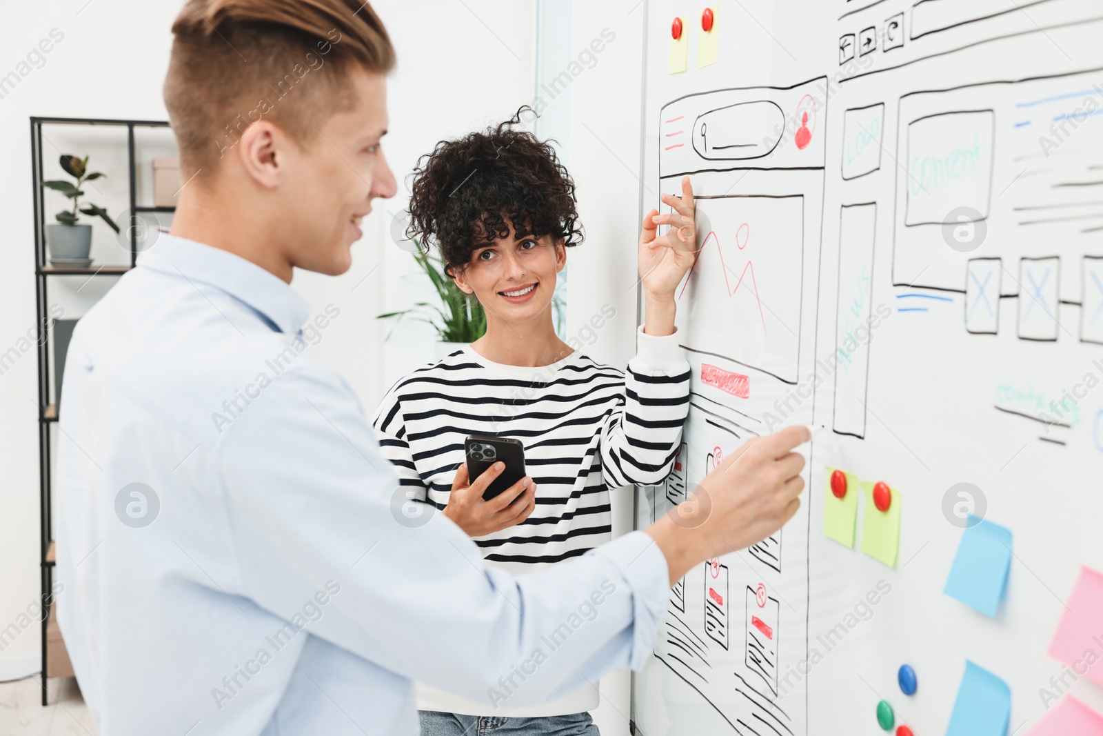 Photo of Developing UI design. Man and woman drawing website wireframe on whiteboard indoors