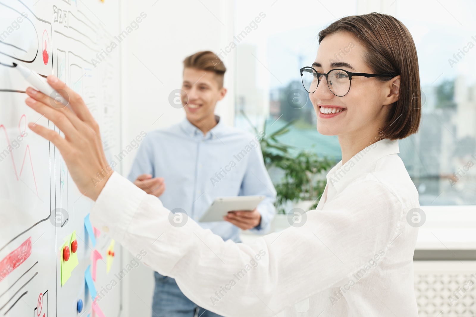 Photo of Developing UI design. Man and woman drawing website wireframe on whiteboard indoors