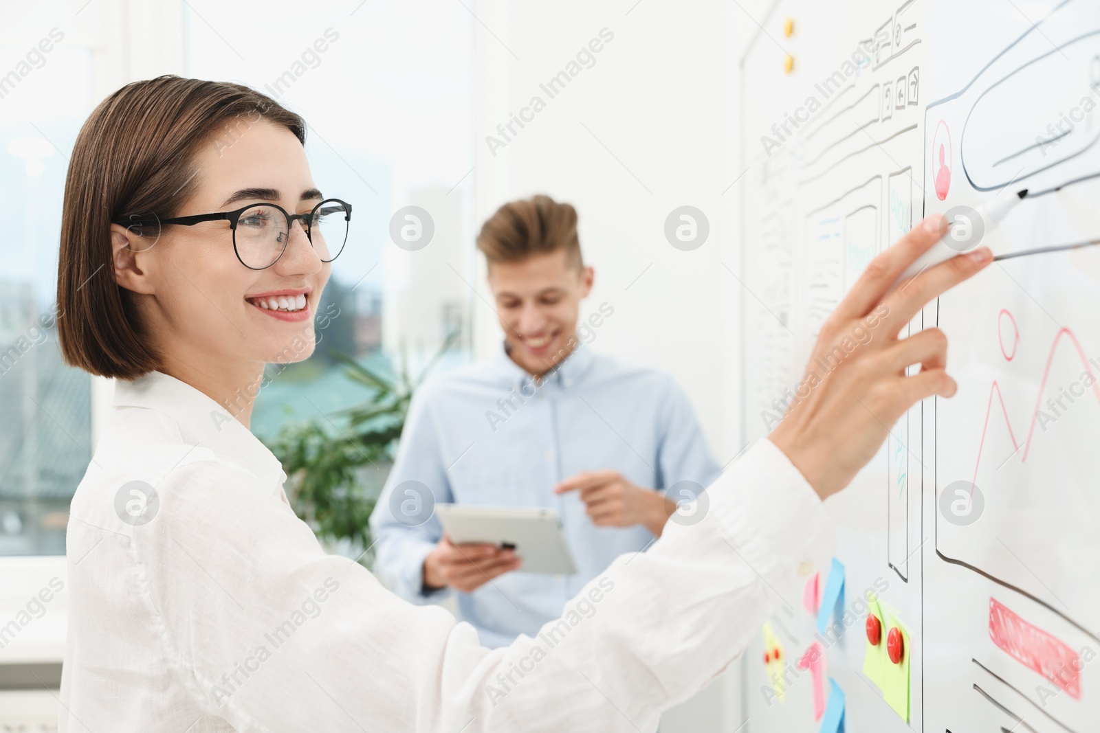 Photo of Developing UI design. Man and woman drawing website wireframe on whiteboard indoors