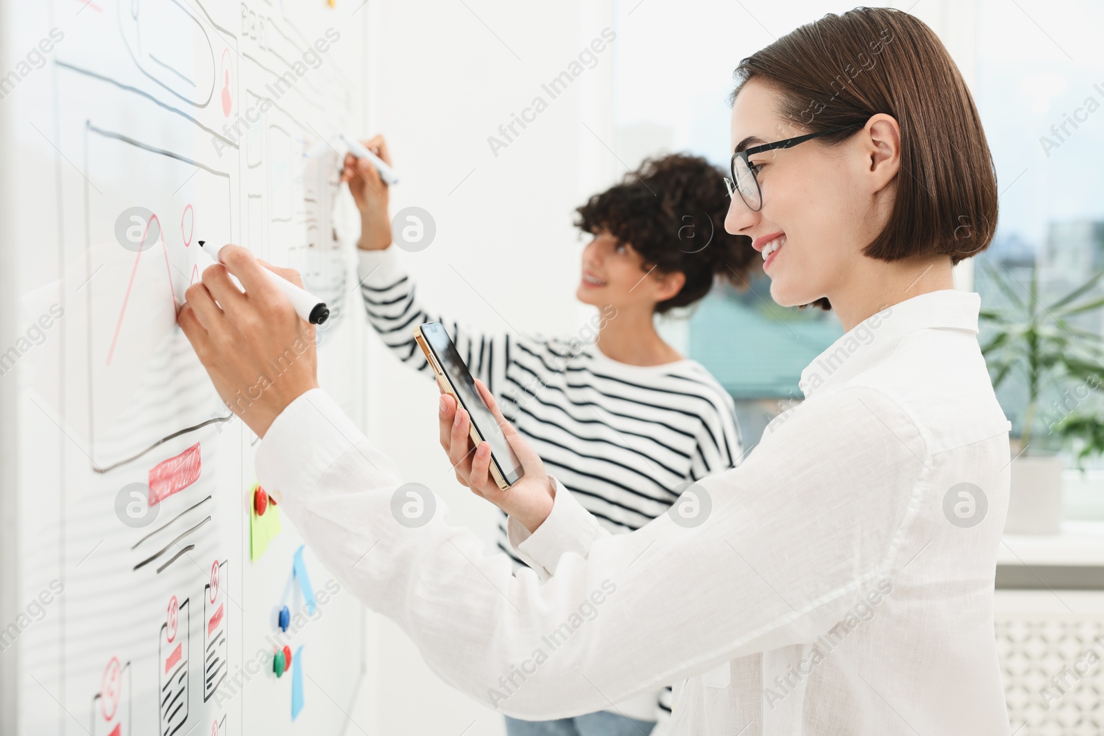 Photo of Developing UI design. Women drawing website wireframe on whiteboard indoors