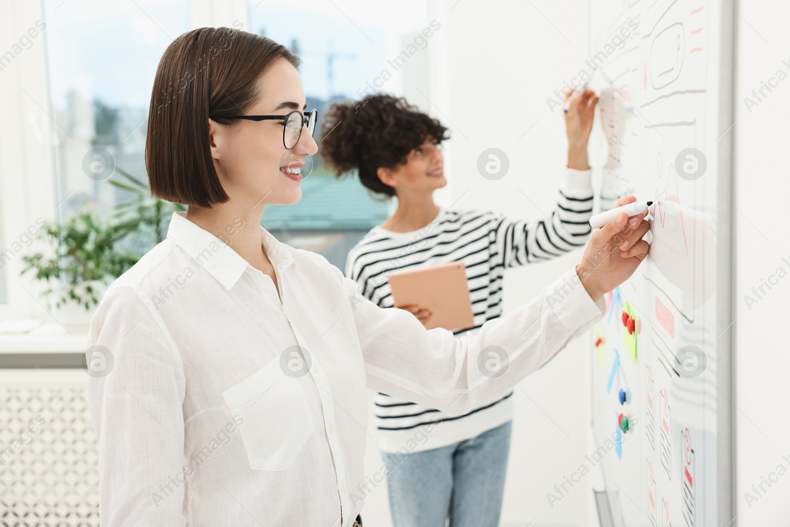 Photo of Developing UI design. Women drawing website wireframe on whiteboard indoors