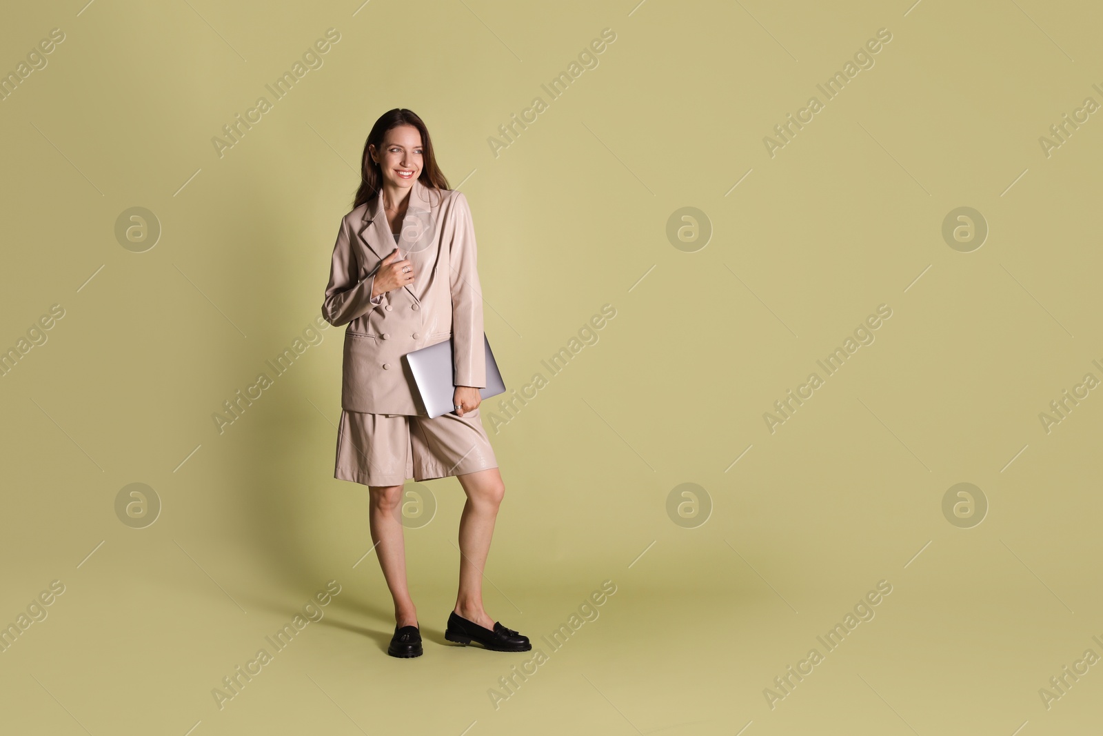 Photo of Beautiful woman in stylish beige suit with laptop on olive background, space for text