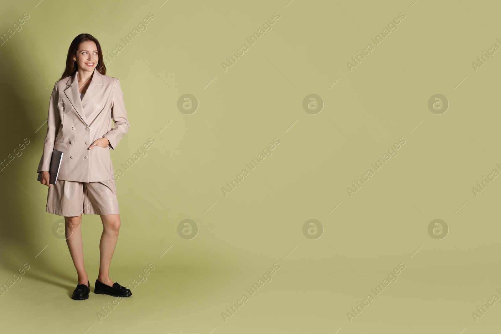 Photo of Beautiful woman in stylish beige suit with laptop on olive background, space for text