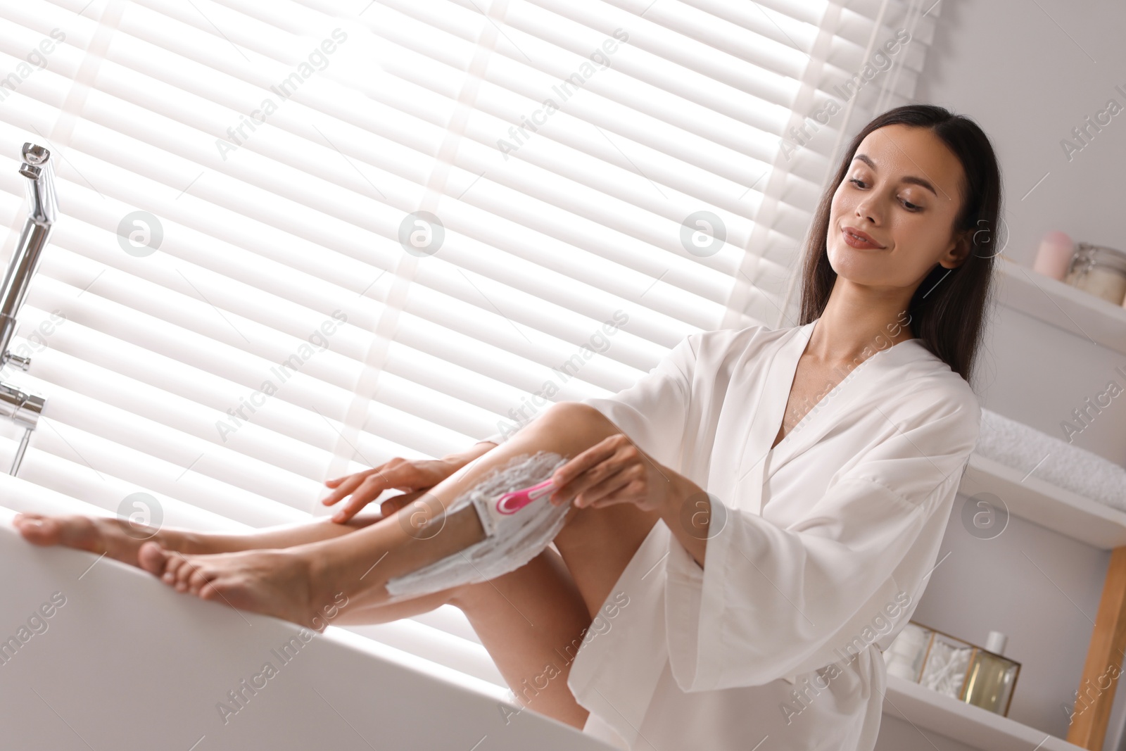 Photo of Beautiful woman shaving leg in bathroom, low angle view