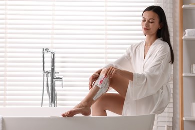 Photo of Smiling woman shaving leg in bathroom. Depilation procedure