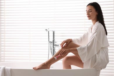 Photo of Beautiful woman shaving leg in bathroom. Space for text