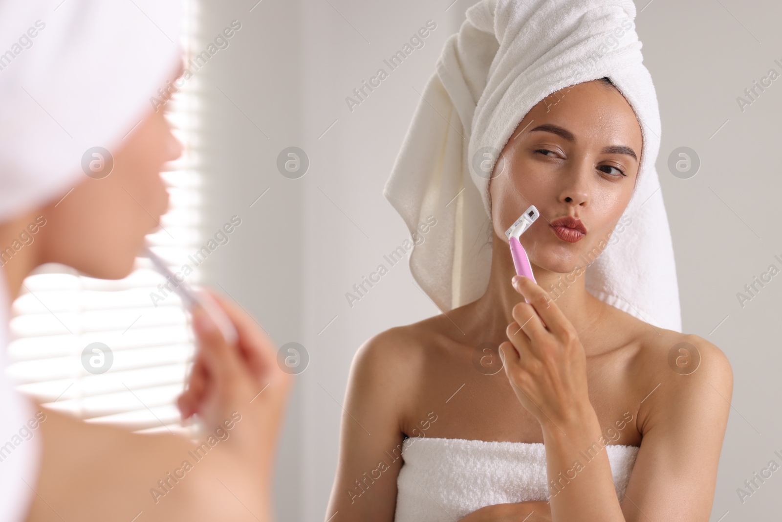 Photo of Beautiful woman shaving face near mirror indoors