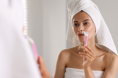 Photo of Beautiful woman shaving face near mirror indoors